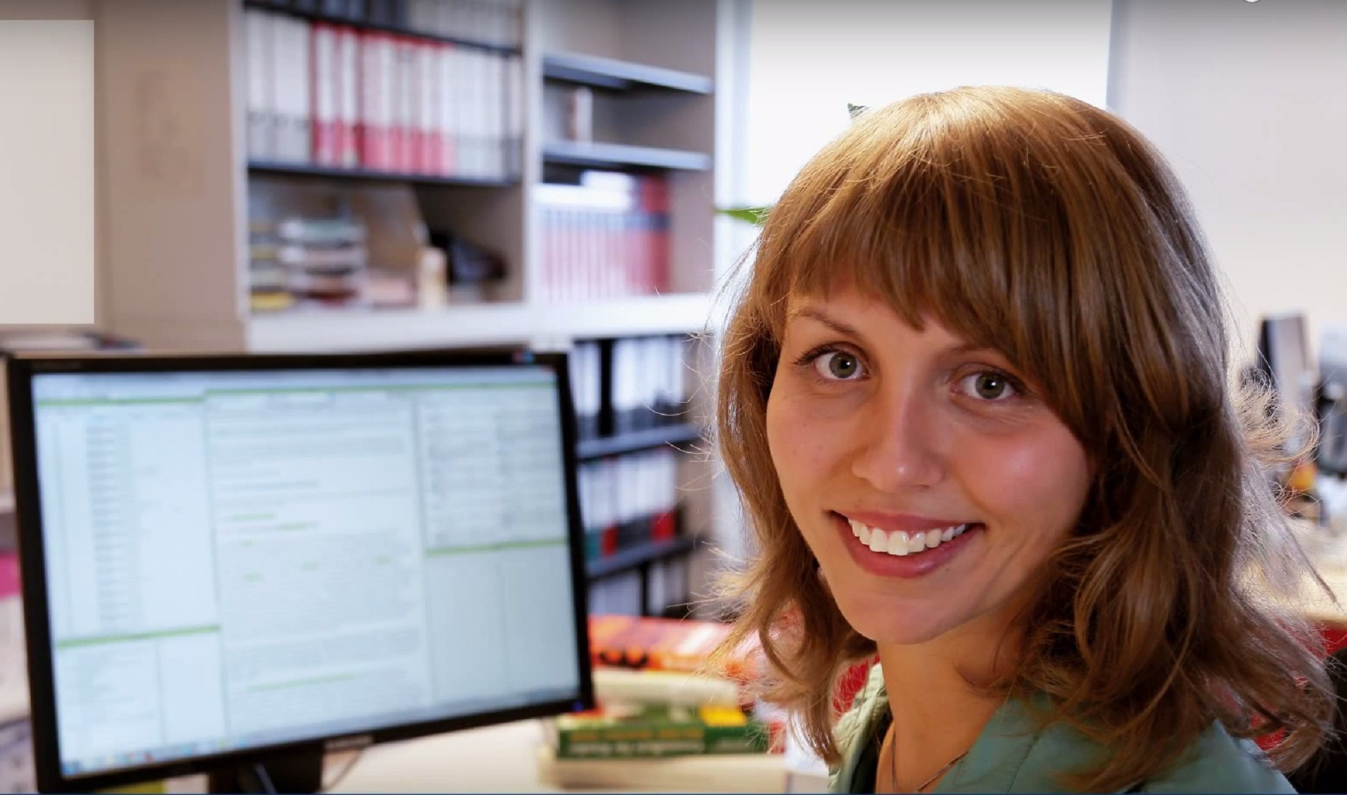 Young woman smiling into the camera with a computer screen of index-manager in her background.